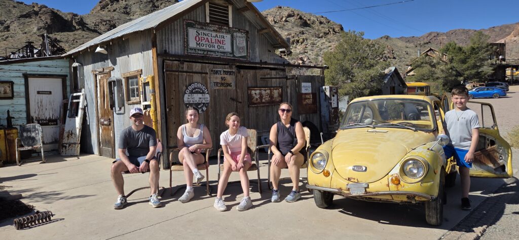 Group by rustic wooden building and vintage yellow car in sunny Nevada ghost town near Las Vegas, perfect for sightseeing tours.