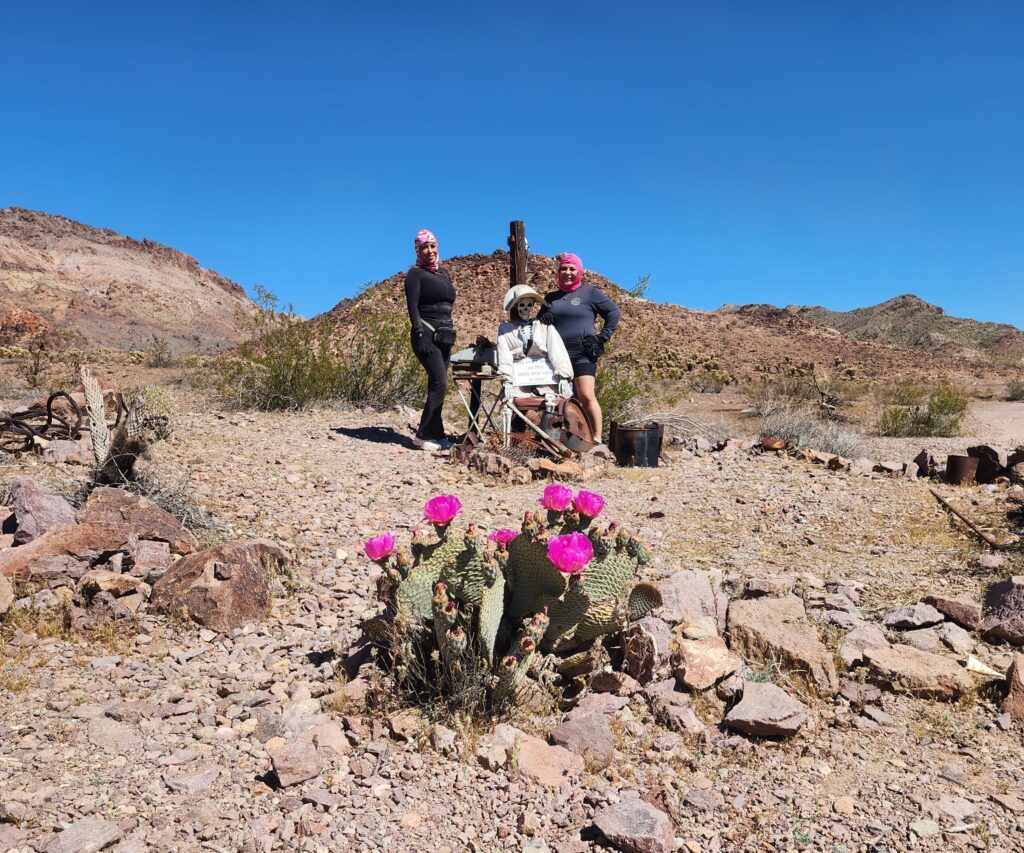 Three people pose by a blooming cactus in Nevada’s rocky desert near Las Vegas, with mountains and clear blue skies behind.