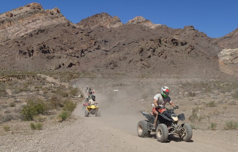 Adventurers ride ATVs on a dusty trail near Nevada’s brown mountains under a blue sky—perfect for Las Vegas ATV tours.