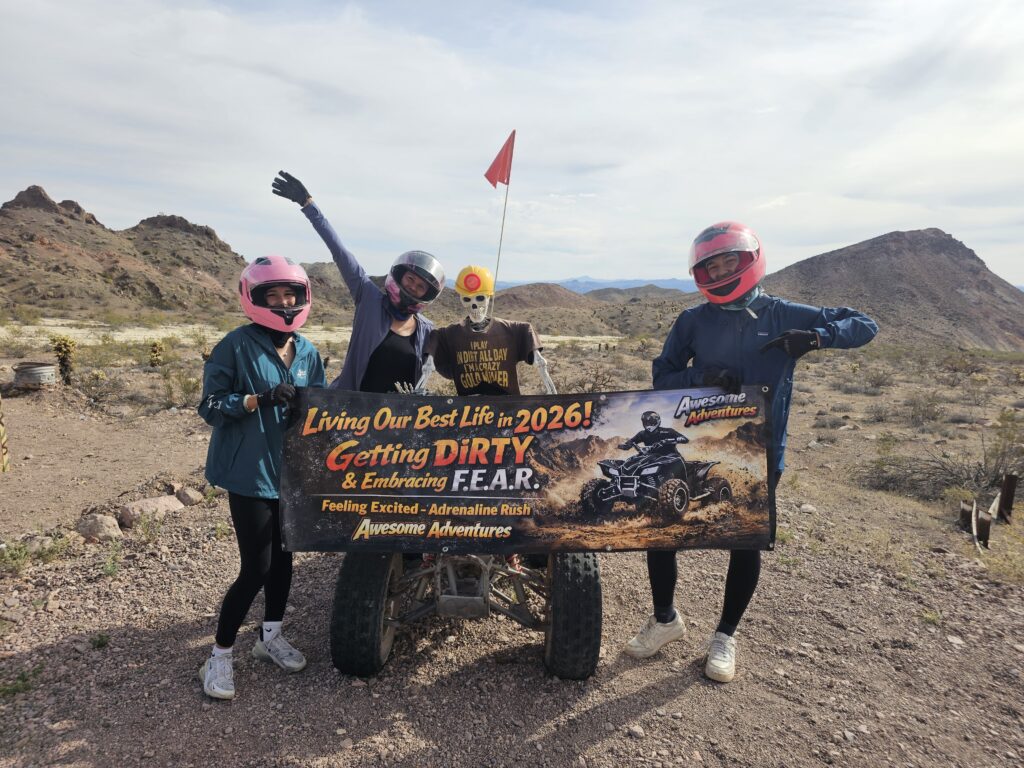 Group in pink helmets and a skull mask with banner in Nevada desert, promoting 2026 RZR rides near Las Vegas and Colorado River.