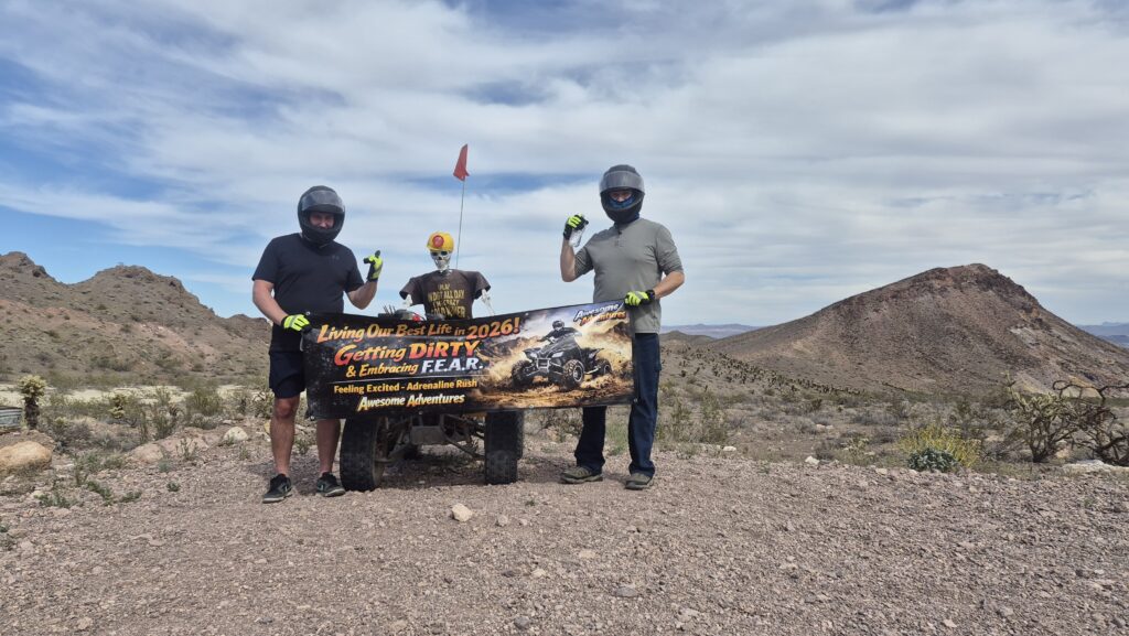 Two adventurers in helmets hold a motivational banner during an ATV tour near Las Vegas, Nevada’s desert hills and Colorado River.