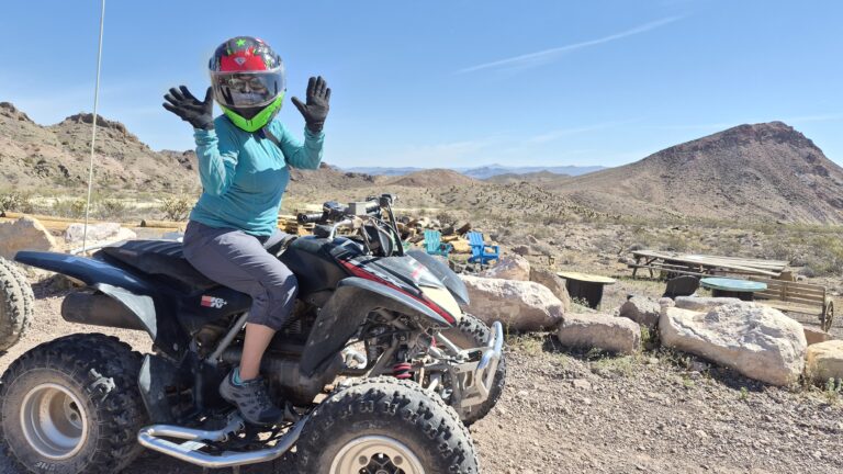 Adventurer in turquoise shirt enjoys ATV tour near Las Vegas, with Nevada desert and mountains under a clear blue sky.