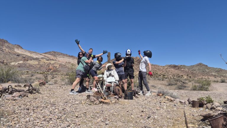 Group in helmets and masks pose with robot figure in Nevada desert near Las Vegas, perfect for ATV tours or Ghost Town sightseeing.