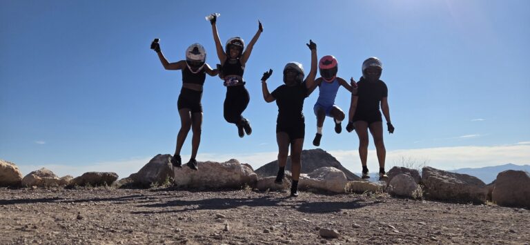 Group wearing helmets and athletic gear jumps on rocky Nevada terrain near Las Vegas after an exciting ATV tour adventure.