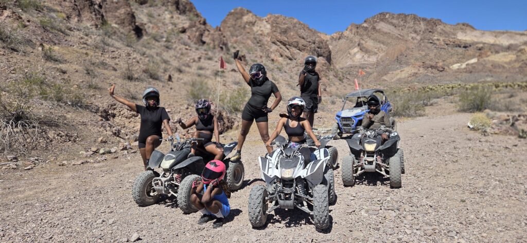 Six riders in helmets pose with ATVs on a Nevada desert trail near Las Vegas, ready for an exciting off-road ATV tour adventure.