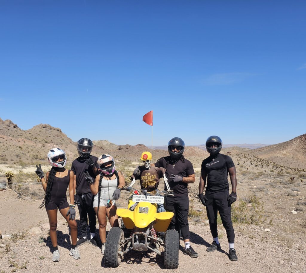 Group in helmets by yellow ATV on Nevada desert tour near Las Vegas, rocky hills, red flag; perfect for ATV and RZR adventures.