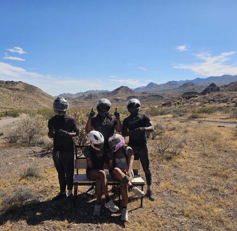 Group in black gear and helmets on Nevada's rocky terrain near Las Vegas, posing after an exciting ATV tour under blue skies.