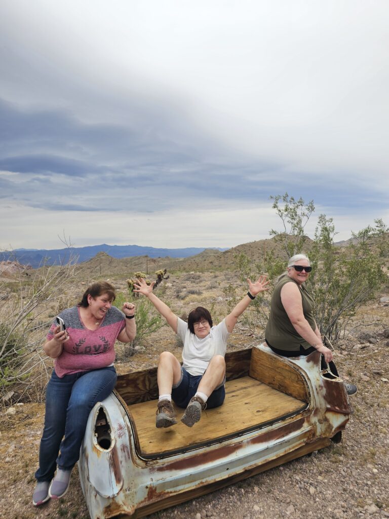 Three friends laugh on a rusty car bench in the Nevada desert near Las Vegas, perfect for Ghost Town sightseeing adventures.