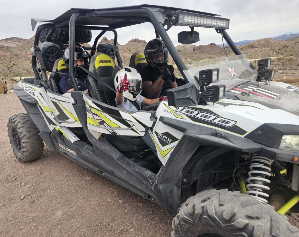 Smiling group in helmets enjoys a Polaris RZR on a Nevada desert ATV tour near Las Vegas, one flashes a peace sign.