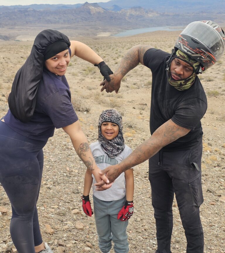 Smiling family poses on Nevada hillside near Colorado River after ATV tour, mountains and lake in background.