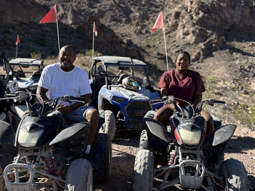 Two people on ATVs with red flags pause on Nevada rocky terrain near Las Vegas mountains, ready for an ATV tour adventure.