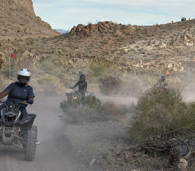 ATV riders explore a dusty Nevada desert trail near Las Vegas, with rocky hills, red flags, and off-road tour adventure views.
