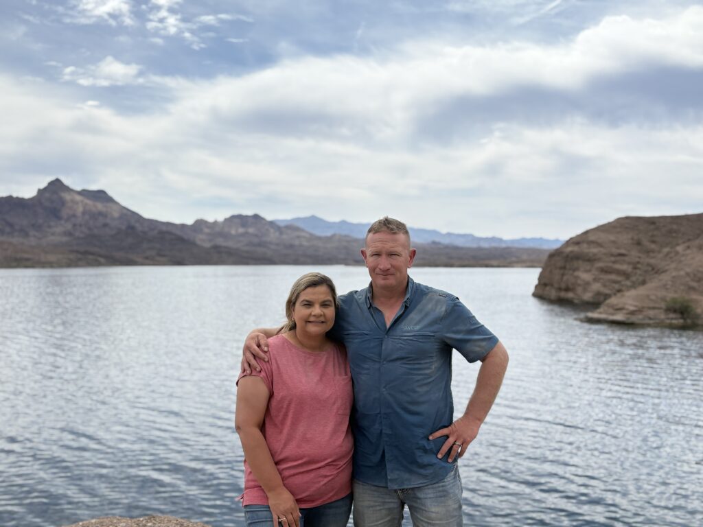 Couple by the Colorado River near Las Vegas, Nevada, with mountains behind; perfect spot for ATV tours on a partly cloudy day.
