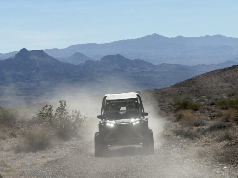 ATV rides near Las Vegas: off-road vehicle on a dusty Nevada trail, rocky hills, sparse desert plants, and distant mountains.