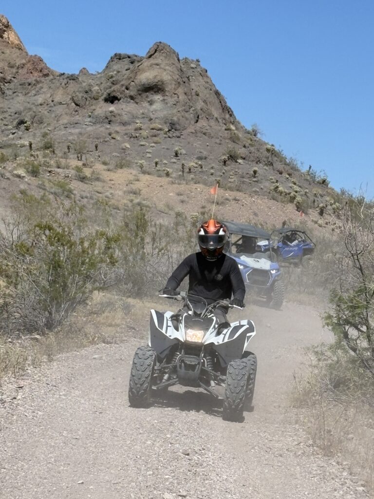 Enjoying an ATV tour near Las Vegas, riders speed along a dusty Nevada trail with rocky hills and clear blue skies in the background.
