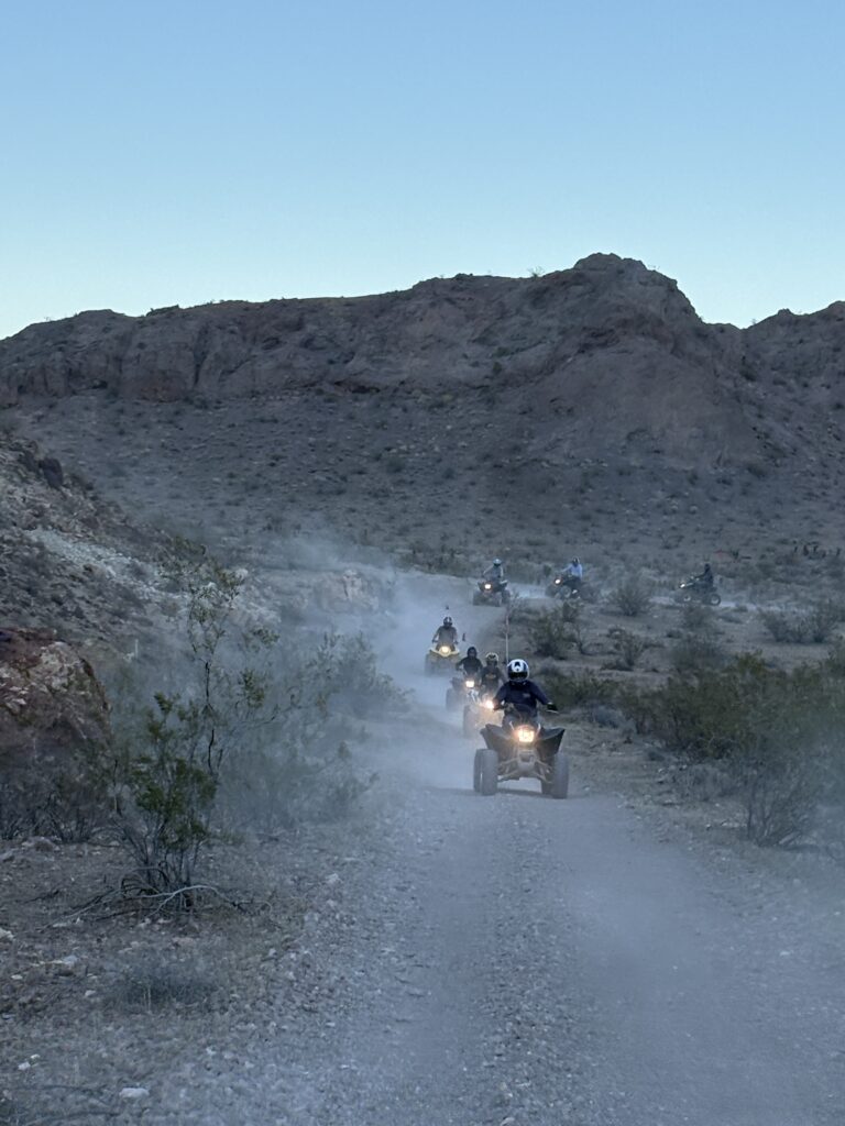 ATV riders explore a dusty Nevada desert trail near Las Vegas, surrounded by rocky hills and sparse brush on an off-road RZR tour.