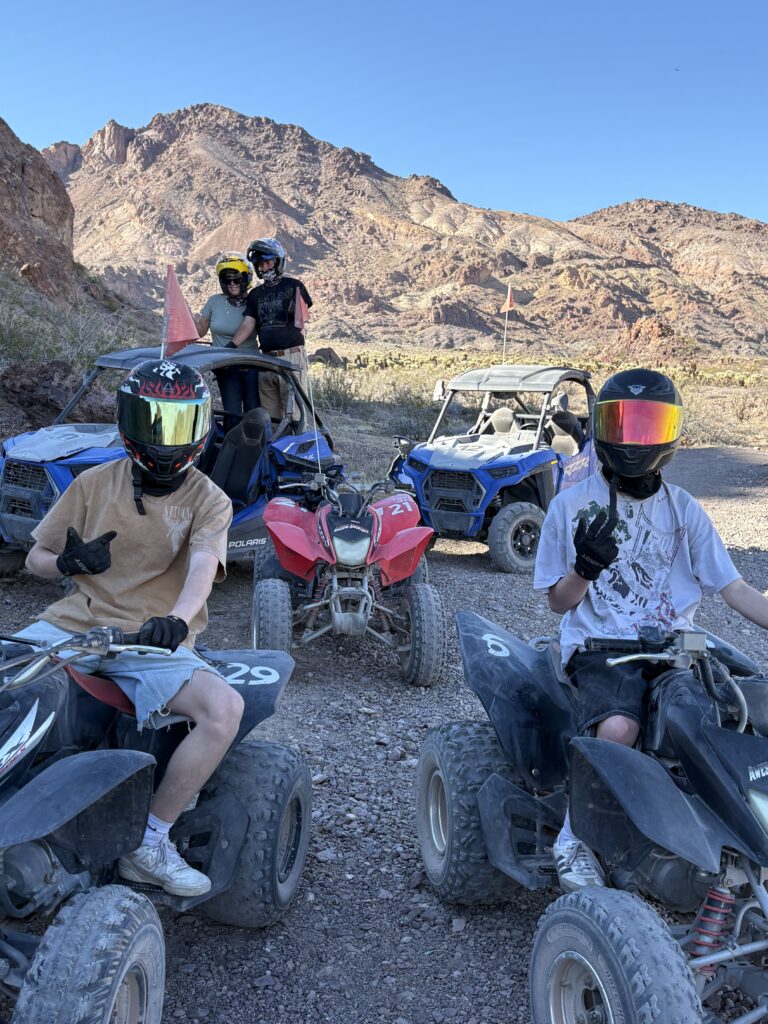 Group wearing helmets on ATVs in Nevada desert near Las Vegas, posing during an ATV tour with mountains in the background.