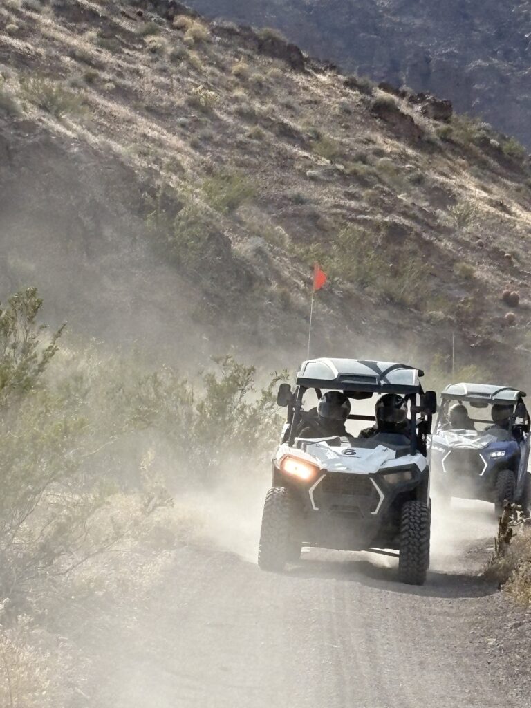 ATVs on a dusty Nevada trail near Las Vegas, with red flag, rocky hills, and desert shrubs—perfect for RZR off-road tours.