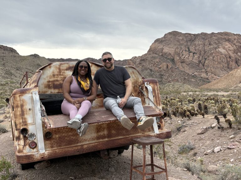 Smiling friends relax on a rusty pickup near Nevada’s rocky desert, perfect for Las Vegas Ghost Town sightseeing adventures.