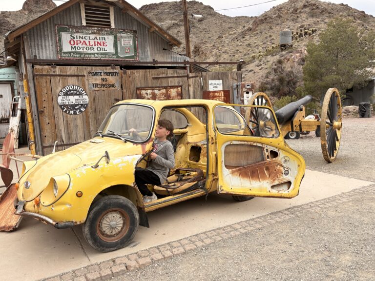 A young boy in a rusty yellow car at a Nevada ghost town near Las Vegas, perfect for sightseeing and Colorado River ATV tours.