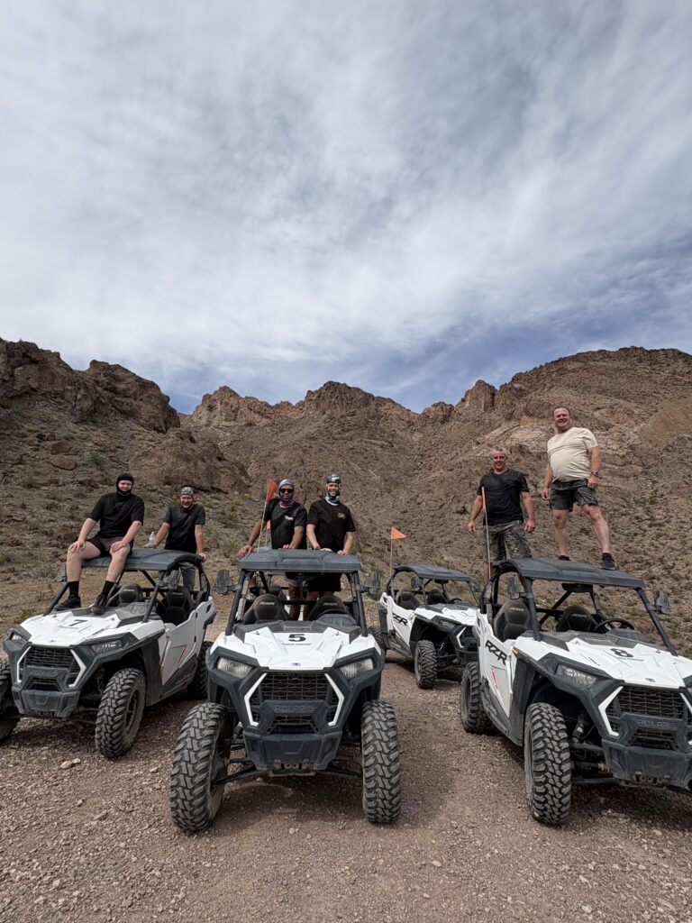 Group poses with five off-road vehicles near Las Vegas in a Nevada desert, ready for ATV tours and RZR rides under blue skies.