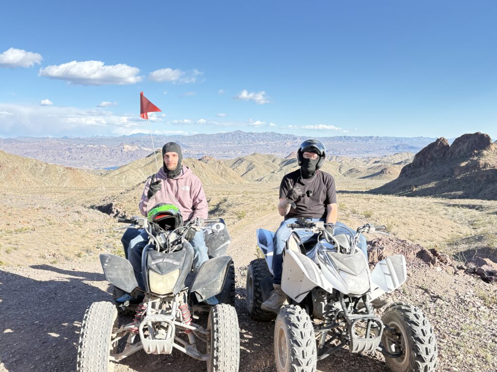 Riders in helmets on ATVs pause on a rocky Nevada trail with desert views near Las Vegas and the Colorado River under blue skies.