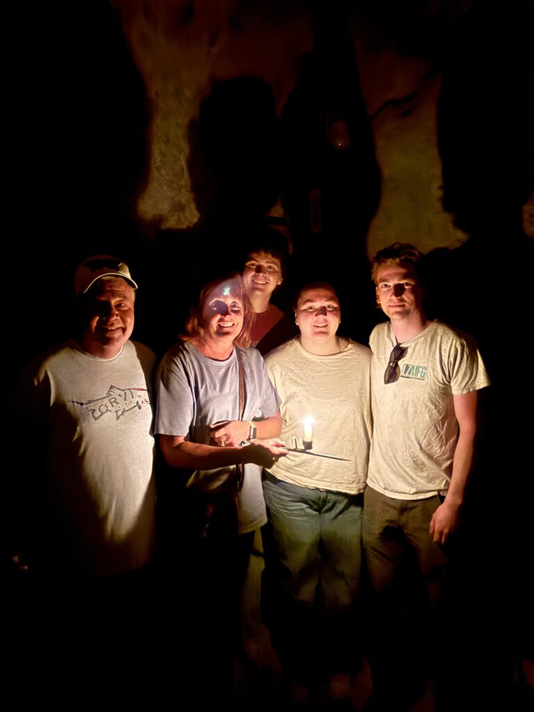 Group smiles in a dark Nevada cave, lit by candle; shadows dance—fun on a Colorado River ATV tour near Las Vegas.