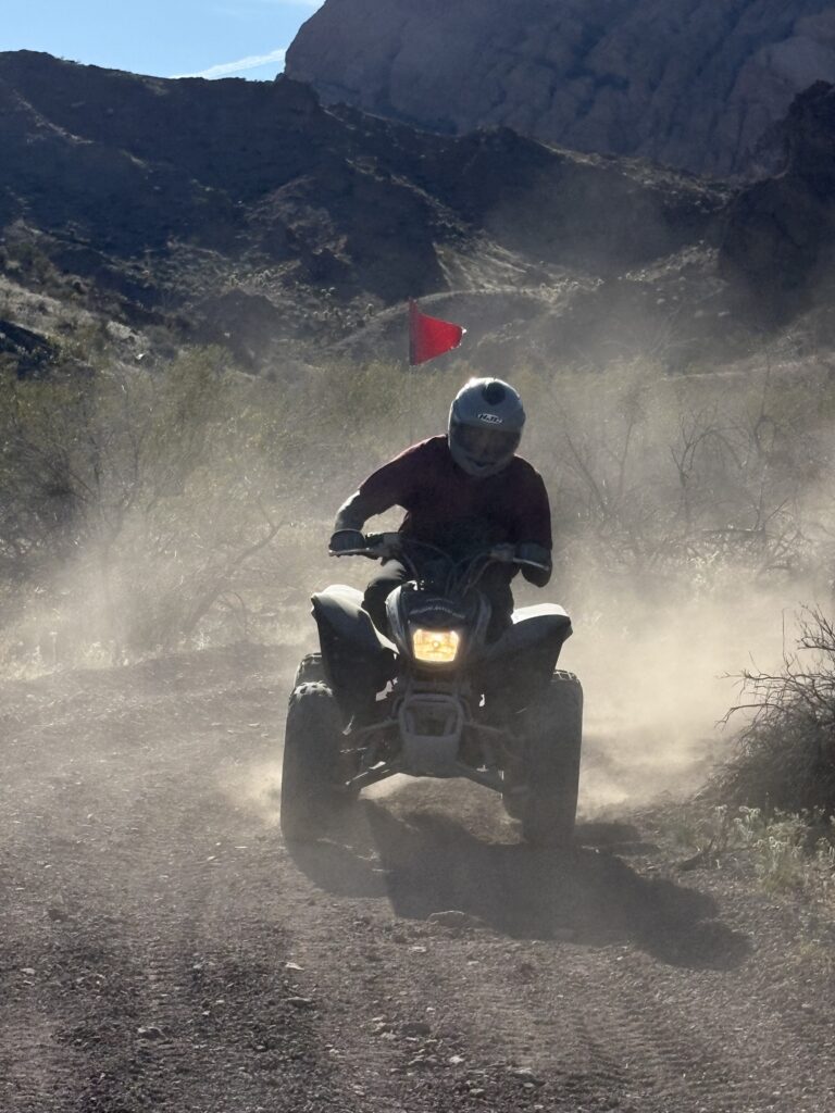 Helmeted rider on ATV tours a dusty Nevada desert trail near Las Vegas, with rocky terrain and red flag in the background.