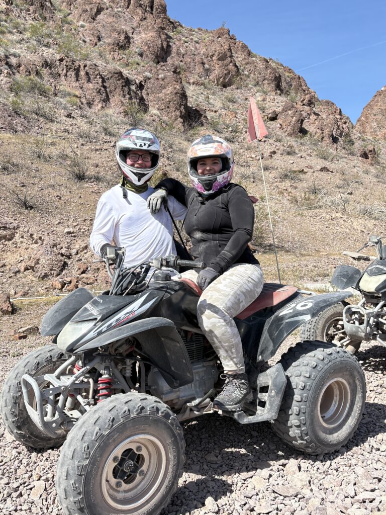 Smiling duo in helmets pose with ATV during a Nevada desert RZR tour near Las Vegas and the Colorado River.