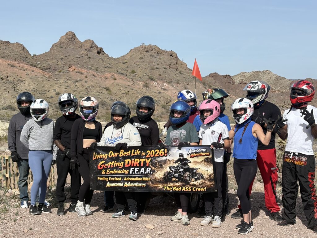 Adventurers in helmets pose by Nevada’s rocky hills, banner reads “Living Our Best Life 2026!” after ATV & Ghost Town tours.
