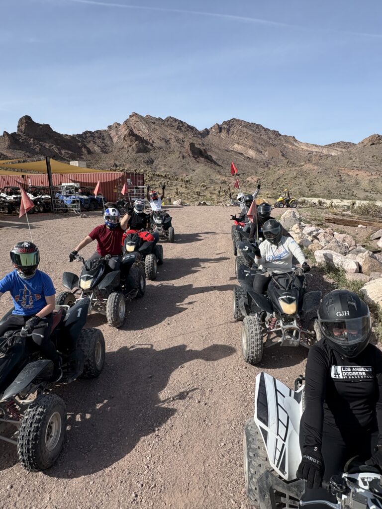 Group on ATVs with helmets prepare for a Nevada desert ATV tour near Las Vegas, with rocky mountains in the background.