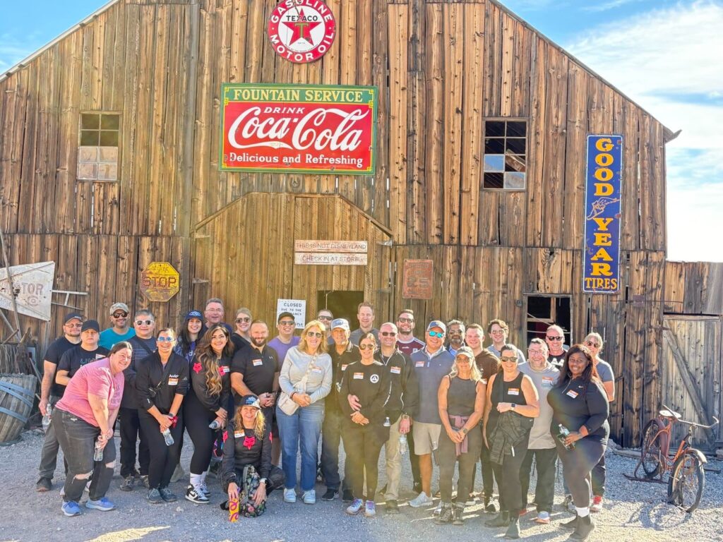 Smiling group at Nevada ghost town near Las Vegas, in front of rustic building with vintage signs, dog, and bicycle—perfect for sightseeing.