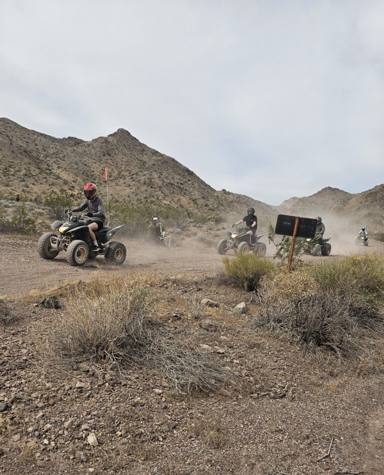 Riders enjoy an ATV tour on a dusty Nevada desert trail near Las Vegas, with rugged hills and a weathered sign along the path.