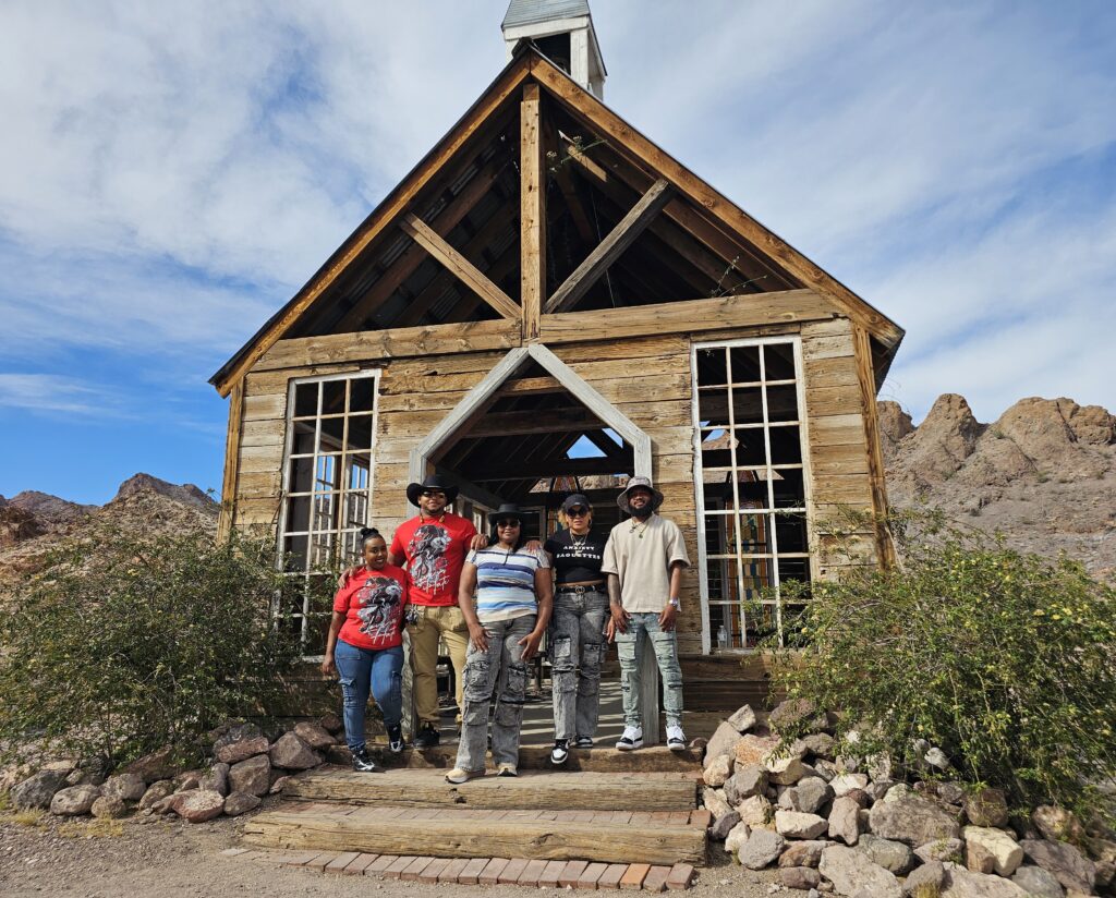 Group poses before a rustic wooden building in a Nevada ghost town near the Colorado River, perfect for ATV tours and sightseeing.