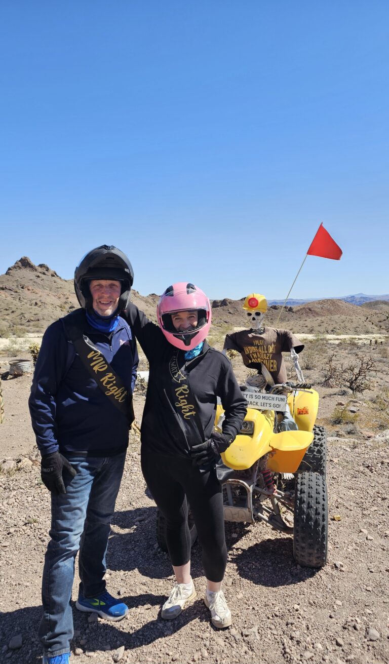 Couple with MR Right/MRS Right sashes pose by ATVs on a Nevada desert Las Vegas ATV tour, another rider in background.