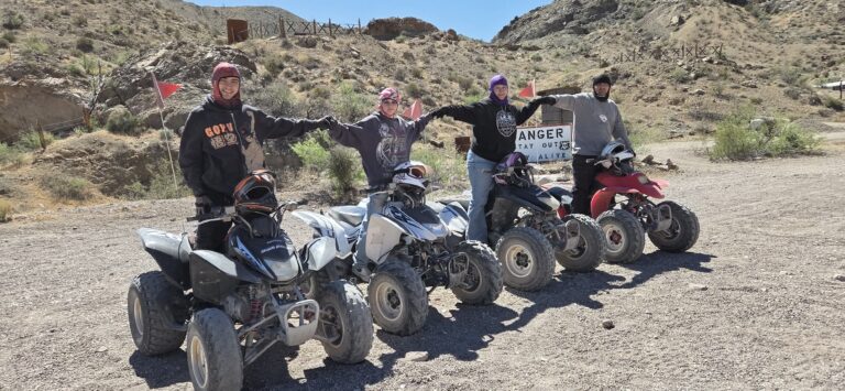 Group near parked ATVs in Nevada desert, smiling by Danger sign—enjoying Las Vegas ATV tour and Colorado River views.