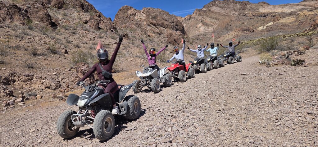 Group enjoying an ATV tour near Las Vegas, Nevada, riding on rocky trails with mountains behind, raising arms in joyful excitement.