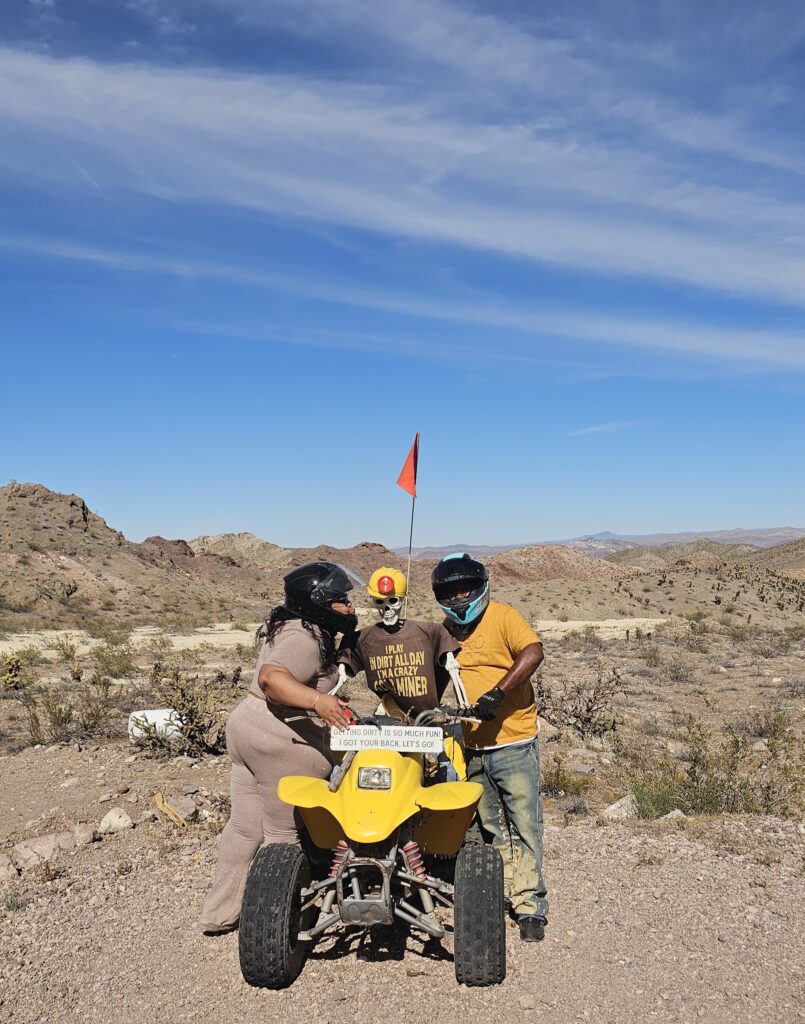 Two people in helmets by a yellow ATV, ready for an ATV tour in Nevada’s rocky desert near Las Vegas under a blue sky.