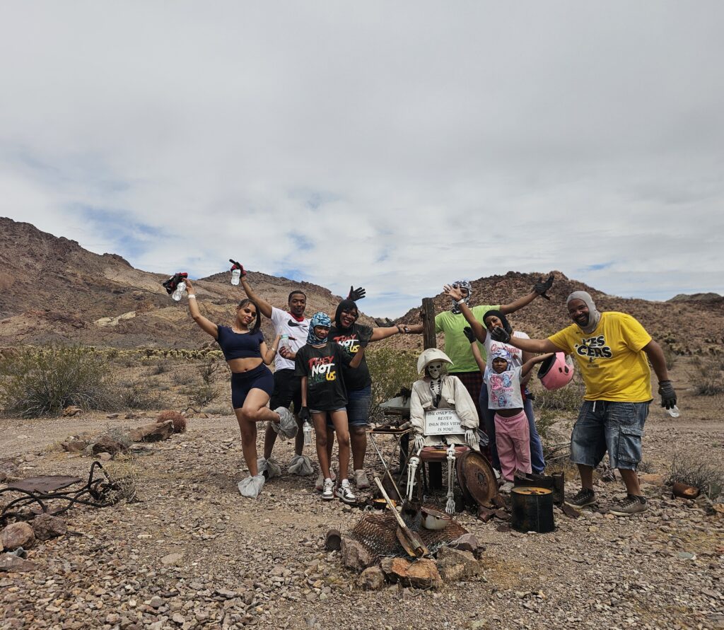 Six friends with raised arms pose by a mannequin in Nevada’s rocky desert, enjoying an ATV tour adventure near Las Vegas.