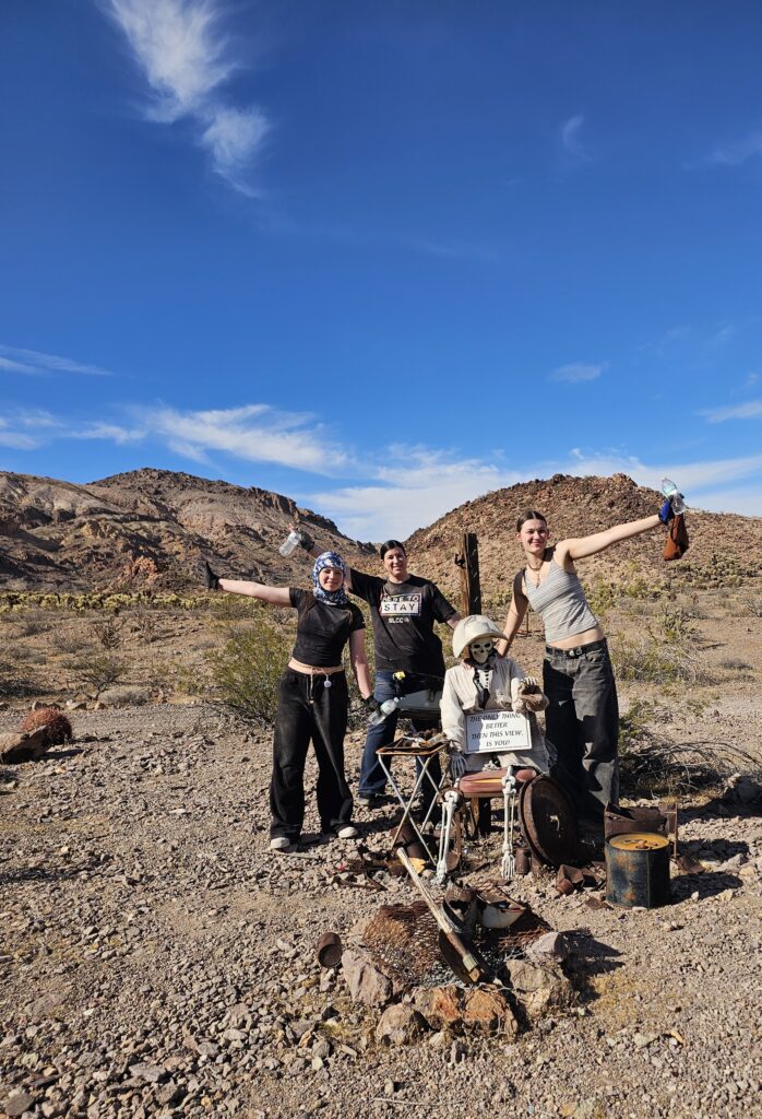 Three people pose with a mannequin near Las Vegas in a rocky Nevada desert, blue sky, mountains—perfect for ATV or Ghost Town tours.