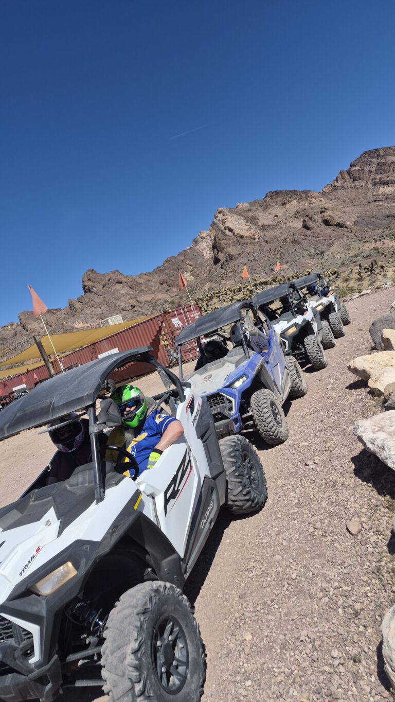 ATV tour near Las Vegas: riders in helmets on a Nevada desert trail, with Ghost Town sights and mountains in the background.