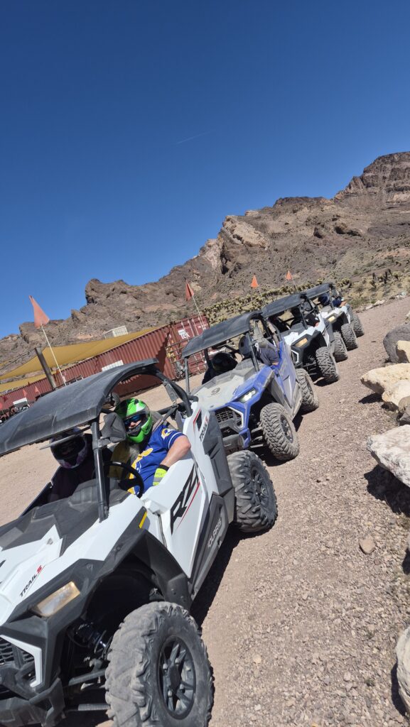 ATV tour group with helmets and goggles parked on rocky Nevada desert terrain near Las Vegas, mountains, and blue sky.