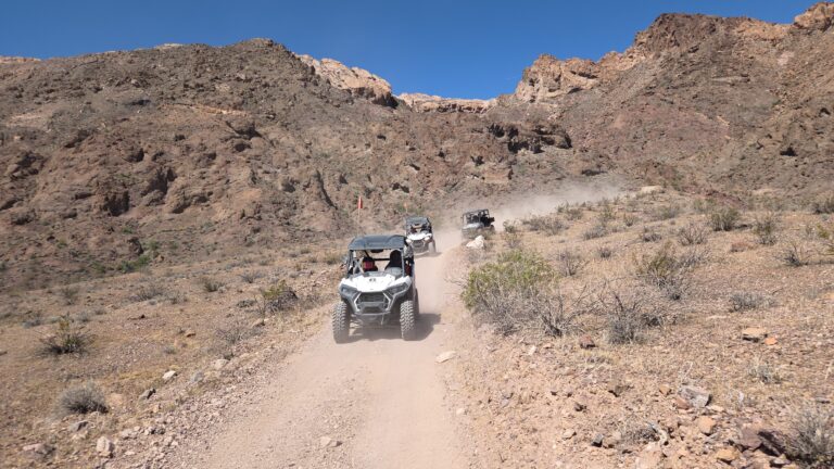 ATV tours near Las Vegas: Three off-road vehicles on a dusty Nevada trail with rocky hills and sparse desert vegetation.