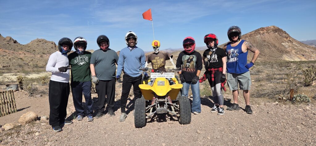 Seven people in helmets by a yellow ATV in the Nevada desert near Las Vegas, ready for an exciting ATV tour adventure.