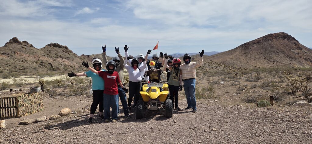 Adventurers in helmets pose by a yellow ATV amid Nevada's rocky desert on a Las Vegas ATV tour near the Colorado River.