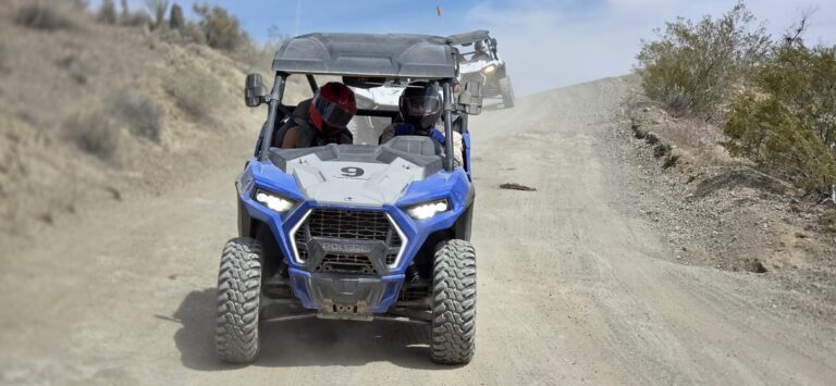 Experience thrilling RZR off-road rides near Las Vegas as two helmeted adventurers explore Nevada’s desert trails in a blue Polaris.