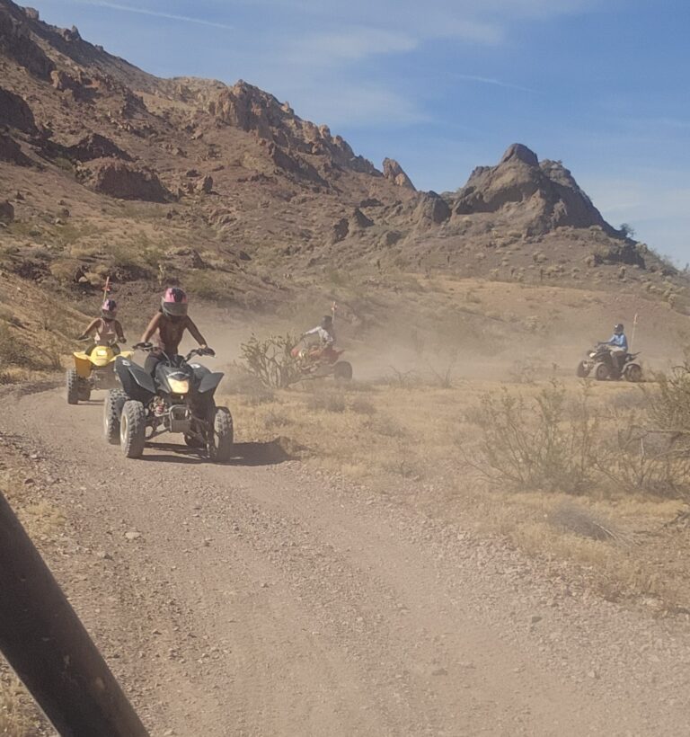 ATV riders traverse a dusty Nevada desert trail near Las Vegas with rocky hills, blue sky, and Colorado River views.