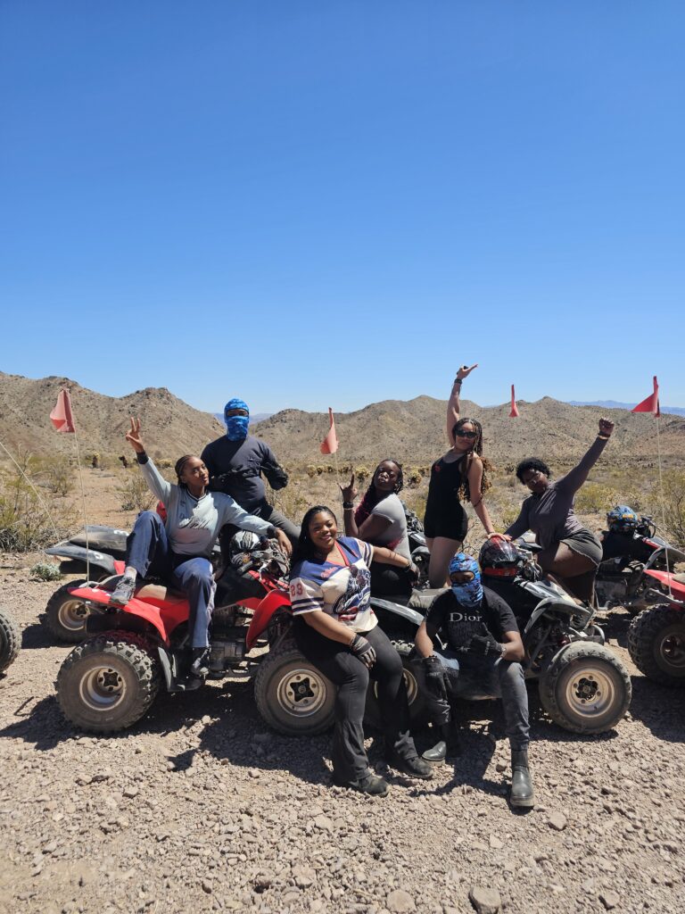 Smiling group on ATVs along a rocky Nevada trail near Las Vegas, posing for an ATV tour with red flags, mountains in the background.