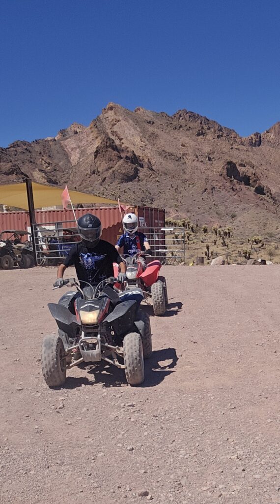 ATV riders with helmets explore a dusty Nevada trail near the Colorado River, mountains, and Las Vegas Ghost Town attractions.