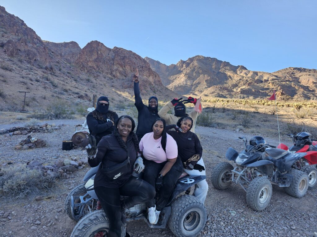 Group enjoys a Nevada ATV tour near Las Vegas, posing on two ATVs in a rocky desert with mountain views and adventure vibes.